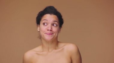 Afro-Amerikalı genç bir kadının omuz silkme ve şaşkın bakışlarla söylediği güzel bir portre. Kahverengi stüdyo arka planında poz veren siyah bir kadın model. Yavaş çekim hazır, 4K 59.94fps 'de..