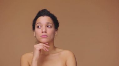 Genç Afrikalı Amerikalı bir kadının güzel portresi bir şey düşünüyor, aklına gelen bir fikir onu neşelendiriyor. Siyah kadın, kahverengi stüdyo arka planında poz veriyor. Yavaş çekim hazır, 4K 59.94fps 'de.