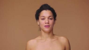 Kendisiyle gurur duyan ve kendini gösteren Afrikalı Amerikalı genç bir kadının güzel portresi. Ben buyum. Kahverengi stüdyo arka planında poz veren siyah bir kadın model. Yavaş çekim hazır, 4K 59.94fps 'de..