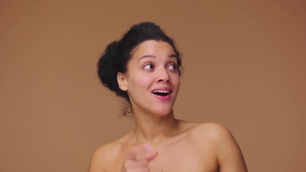 若いアフリカ系アメリカ人女性の美しさの肖像画は、何か、鼻や親指のようなものを指しています。黒の女性は茶色のスタジオの背景にポーズ。スローモーション準備完了、 59.94fpsで4K — ストック動画