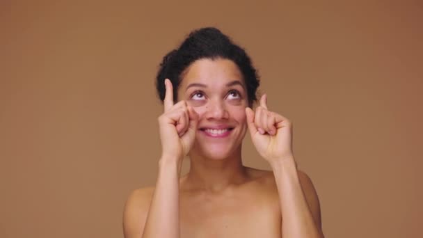 若いアフリカ系アメリカ人女性の美しさの肖像画は、その後何かのために手を指して、親指を示しています。黒の女性は茶色のスタジオの背景にポーズ。スローモーション準備完了、 59.94fpsで4K — ストック動画