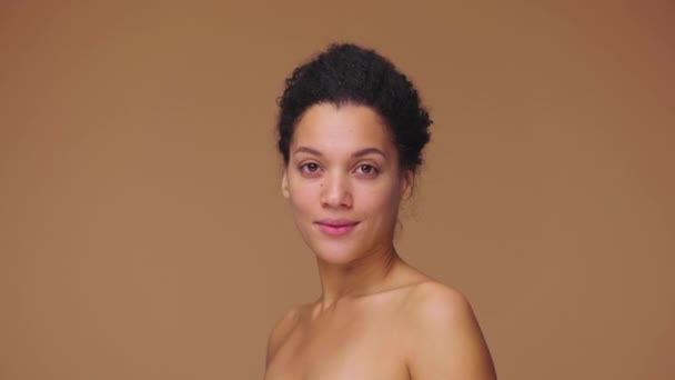 Portrait de beauté de la jeune femme afro-américaine se tourne vers la caméra et sourit, montrant des dents blanches. Modèle féminin noir posant sur fond de studio brun. Prêt au ralenti, 4K à 59.94fps. — Video