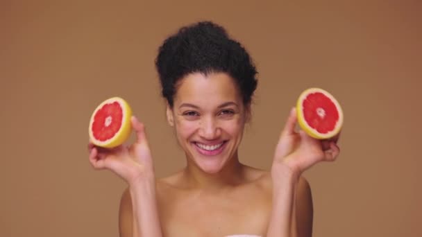 年轻的非洲裔美国女人的美丽画像，开开开心心，用一半的柚子遮住眼睛。黑色女性在棕色工作室背景。慢动作准备，4K，59.94fps. — 图库视频影像