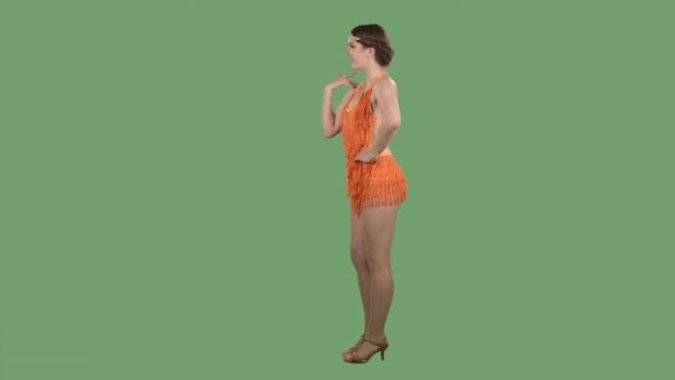 Side view of a charming young woman flirtatiously waving her hand and gesturing for you to come here. Girl in an orange dress with fringes on a green screen in the studio. Slow motion. — Stock Video