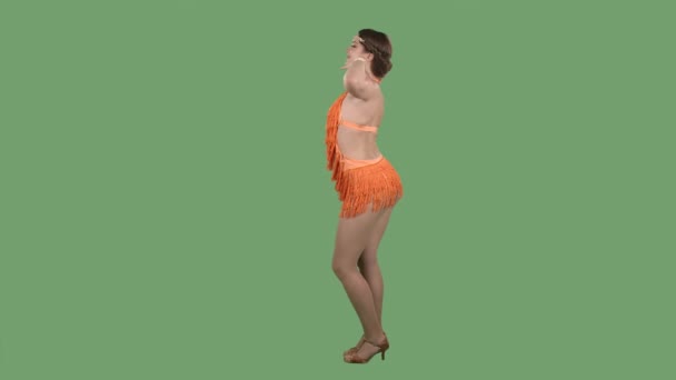 Seitenansicht einer anmutigen und plastischen jungen Frau, die kokett lächelt und tanzt. Brennende Brünette in einem orangefarbenen Fransenkleid auf einer grünen Leinwand im Studio. Zeitlupe. — Stockvideo