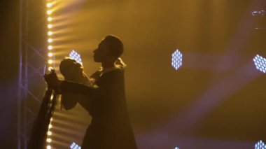 Profesyonel balo dansçıları karanlık bir stüdyoda parlak ışıkların önünde dans ediyorlar. Erkek ve kadın dans partnerleri baloda dans ediyor. Siluetler. Kapat..