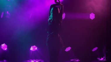 İnce bir kadının silueti rumba dansı yapıyor. Bir balo dansçısı, mavi-mor ışıklı karanlık bir stüdyonun dumanlı arka planına karşı tutkuyla dans eder. Kapat..