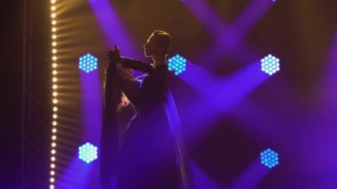 Vals yapan sevimli bir çiftin siluetleri. Bir adam partnerini dansa davet eder ve onunla siyah arka planda parlak mavi ışıklarla karanlık bir stüdyoda vals yapar. Kapat..