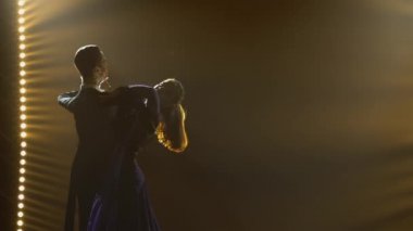 Profesyonel balo dansçılarının klasik valsi. Genç adam ve kadının siluetleri dans adımları atıyorlar, karanlık bir stüdyoda sahne ışıkları ve dumanla sahne alıyorlar. Kapat..