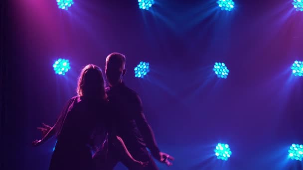 Quelques jeunes danseurs dansent une danse latino-américaine passionnée. Rumba, samba, cha-cha-cha, jive. Silhouettes de deux danseurs sur un fond sombre studio fumé avec des lumières bleu-violet. Gros plan. — Video