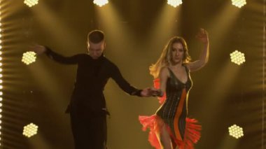 Yangın çıkaran rumba, balo dansında erkek ve kadın partnerler tarafından icra edildi. Karanlık bir stüdyoda, parlak sarı ışıklarla tutkuyla dans eden iki dansçı. Kapat..