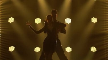 Klasik balo salonu Latin Amerika dansının unsurları profesyonel dansçılar tarafından sahneleniyor. Rumba, samba, cha-cha-cha, jive. Çift siluetleri sarı ışıklarla karanlık stüdyoda dans ediyor.