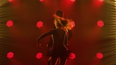 Pasodoble, rumba, samba, cha cha cha. Bir çift dansçı tarafından gerçekleştirilen Latin Amerika danslarının unsurları. Karanlık bir stüdyoda, arka plandaki kırmızı ışıklara karşı bir erkek ve bir kadının siluetleri. Kapat..