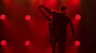 Pasodoble, rumba, samba, cha cha cha. Bir çift dansçı tarafından gerçekleştirilen Latin Amerika danslarının unsurları. Karanlık bir stüdyoda, arka plandaki kırmızı ışıklara karşı bir erkek ve bir kadının siluetleri. Kapat..