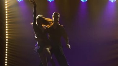 Genç ve güzel dans eden çift dansları cha-cha-cha, rumba, samba. Mavi ışıkları olan karanlık bir stüdyoda dansçıların siluetleri. Kapat..