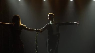 Bir adam ortağının karısıyla vals yapar, onu havada daireler çizer. Baloda, parlak ışık huzmeleriyle aydınlatılmış siluetli bir çift dansçı. Kapat..