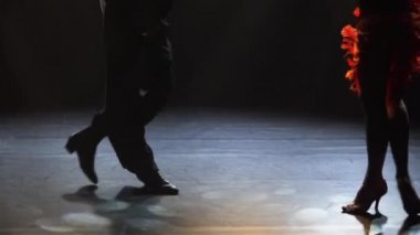 Latin Amerika dansının elementleri balo dansçıları tarafından sahneleniyor. Rumba, cha cha cha, karanlık bir stüdyoda ışık ışınlarıyla klasik balo dansı koreografisi. Siluetler. Bacaklar yakın. Yavaş çekim.