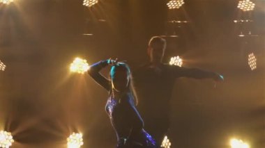 Rumba Drive dansını iki balo dansçısı yapıyor. Takım elbiseli bir adam ve kısa elbiseli bir kadın karanlık stüdyoda parlak ışıkların arkasında neşeyle dans ediyorlar. Siluetler. Kapatın. Yavaş çekim