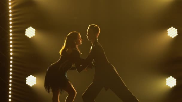 Elementos del baile clásico de salón de baile latinoamericano interpretado por un par de bailarines profesionales. Rumba, samba, cha-cha-cha, jive. Siluetas de pareja bailando de cerca en estudio oscuro con luces amarillas — Vídeos de Stock