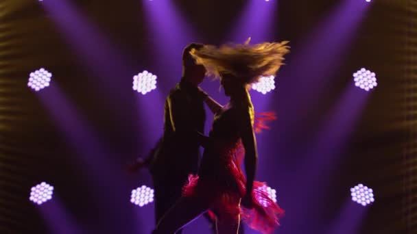 Rumba incendiaire réalisée par des partenaires de danse de salon. Un homme en costume et une femme en robe courte chic dansent passionnément dans un studio sombre aux lumières bleues vives. Des silhouettes. Gros plan. — Video