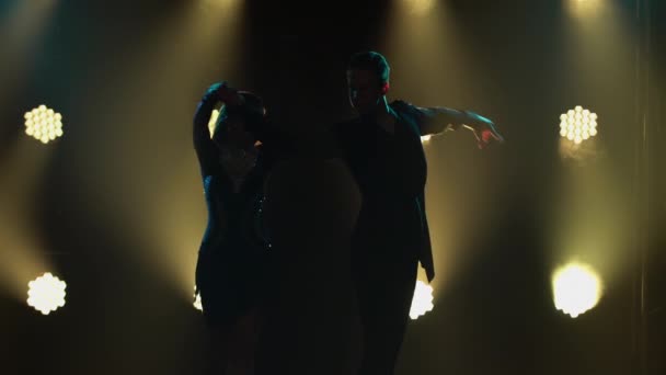 Profesjonalny występ tancerzy towarzyskich w programie tańca latynoamerykańskiego. Sylwetki zmysłowej pary na dymiącym ciemnym tle studia z podświetleniem. Zamknij się.. — Wideo stockowe