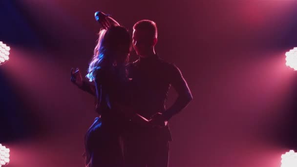 Rumba framförd av ett ungt graciöst par. Silhuetter av dansande partners balsal Latinamerikanska danser mot bakgrund av vinrött ljus i en mörk studio. Närbild. Långsamma rörelser. — Stockvideo