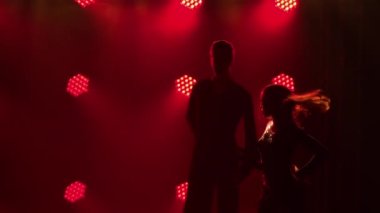 Pasodoble, rumba, samba, cha cha cha. Çift dansçılar tarafından gerçekleştirilen Latin Amerika danslarının unsurları. Karanlık stüdyodaki kırmızı ışıkların arka planına karşı kadın ve erkeğin siluetleri. Kapatın. Yavaş çekim.