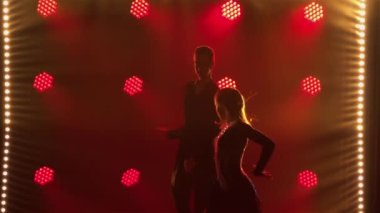 Pasodoble, rumba, samba, cha cha cha. Çift dansçılar tarafından gerçekleştirilen Latin Amerika danslarının unsurları. Karanlık stüdyodaki kırmızı ışıkların arka planına karşı kadın ve erkeğin siluetleri. Kapatın. Yavaş çekim.