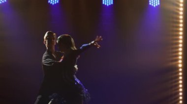 Genç ve güzel dans eden çift dansları cha-cha-cha, rumba, samba. Mavi ışıkları olan karanlık bir stüdyoda dansçıların siluetleri. Kapatın. Yavaş çekim.