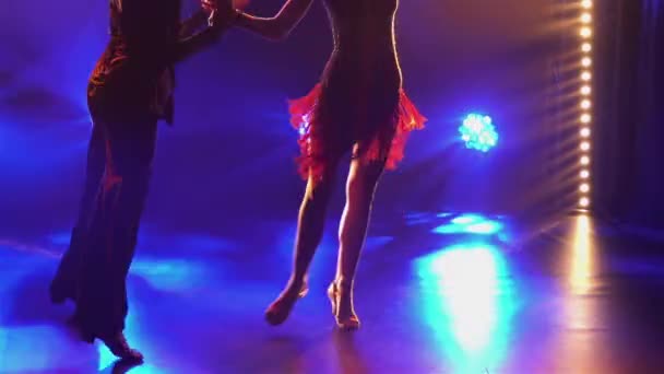 Elementos Danza latinoamericana interpretada por bailarines de salón. Rumba, cha cha cha cha, coreografía clásica de baile de salón en estudio oscuro con rayos de luz de colores. Silueta. Las piernas cierran. Movimiento lento — Vídeos de Stock