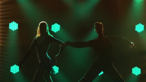 Rumba, samba, cha-cha-cha, jive. Een paar professionele dansers die hartstochtelijk dansen in een donkere studio tegen een achtergrond van groene neonlichten. Silhouetten. Sluit maar af. Langzame beweging. — Stockvideo