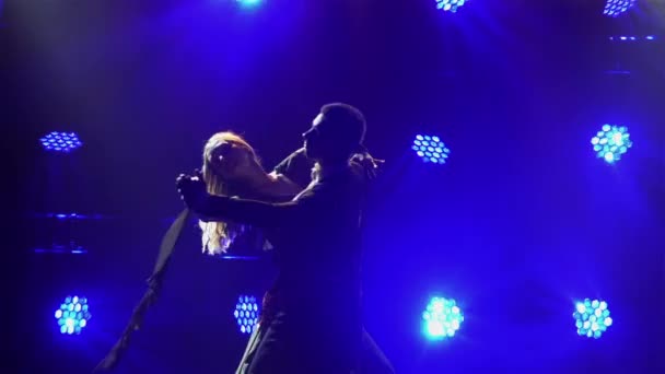 Silhouette of men and women in elegant outfits waltzing in a dark studio. A romantic couple is dancing a classic waltz choreography against the backdrop of blue lights. Close up. Slow motion. — Stock Video