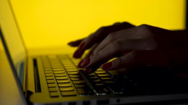 Stüdyoda sarı arka planda dizüstü bilgisayarda çalışan bir kadın. Dizüstü bilgisayarda yazan kadın eli ve parmaklarını kapat. Klavyeye yazı yazmak, bir iş mektubu yazmak. Yavaş çekim.