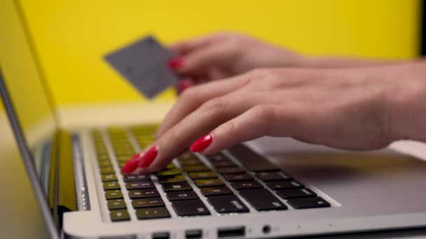 Kobieta używa laptopa do zakupów i płacenia kartą kredytową w studio na żółtym tle. Zbliżenie dziewczyny trzymającej kartę kredytową i wpisującej informacje na laptopie. Zwolniony ruch. — Wideo stockowe