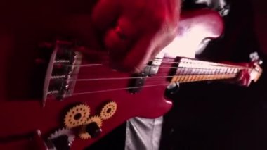 Kırmızı bas gitar çalan erkek ellerinin detaylı makro görüntüsü. Adam tellere parmaklarıyla dokunur ve enerjik bir melodi çalar. Rock konseri, canlı performans, heavy metal. Telli gitar. Yakın çekim..