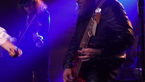 Concierto en vivo enérgico de una banda de rock. Un equipo de músicos toca dinámicamente el violín, el bajo y la batería en la oscuridad entre el humo y la luz azul. Silueta. De cerca.. — Vídeo de stock