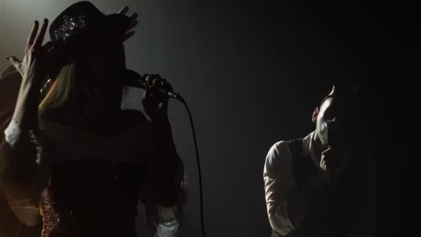 Cantante emocionalmente grita en el micrófono en el rendimiento de la banda de rock. La mujer canta, mientras que los hombres tocan instrumentos musicales. Cool concierto de rock en vivo entre luces dinámicas en la oscuridad. Siluetas. De cerca.. — Vídeo de stock