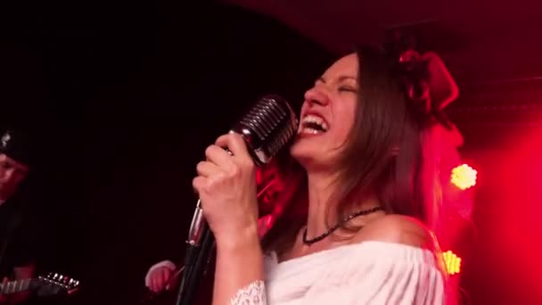 Emocional actuación en vivo de vocalista femenina con banda de rock. Grupo de músicos toca instrumentos y canta en el micrófono en el estudio oscuro sobre un fondo de luces rojas. De cerca.. — Vídeos de Stock