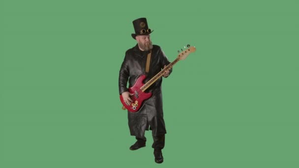 Un uomo barbuto con un lungo cappotto di pelle e un cappello in stile irlandese suona la chitarra rossa. Musicista rock suona il basso in studio sul tasto chroma schermo verde. Rallentatore. — Video Stock