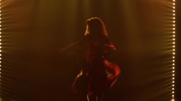 Eine leidenschaftliche Frau im Zigeunerkostüm wirbelt tanzend und schwenkt ihren langen Rock. Eine Tänzerin ist in einem Zigeunervolkstanz in einem dunklen, verrauchten Studio mit gelbem Licht zu sehen. Nahaufnahme. — Stockvideo