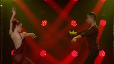 Balo dansı yapan genç dansçılar. Rumba, salsa, tango, flamenko. Dans partnerleri karanlıkta kırmızı spot ışıklarının önünde tutkuyla dans ederler. Kapat..