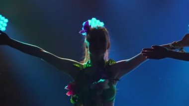 Sevimli bayan dansçı Hawaii dansı yapıyor, vücutlarını ve kalçalarını sallıyor. Hawaii parti luau 'sunda renkli ışıkların önünde dans eden kadın silueti. Kapatın. Yavaş çekim.