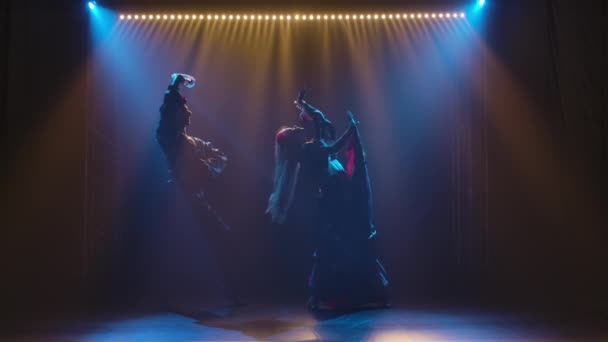 Silueta pareja bailarines en romany ropa bailando en estudio oscuro sobre fondo de luces brillantes. Hombre y mujer bailando apasionadamente danza gitana actuando en el espectáculo teatral. Movimiento lento. — Vídeos de Stock