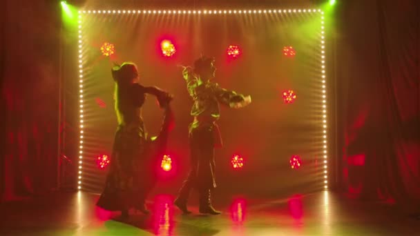 Silueta pareja bailarines en romany ropa bailando en estudio oscuro sobre fondo de luces brillantes. Hombre y mujer bailando apasionadamente danza gitana actuando en el espectáculo teatral. Movimiento lento. — Vídeos de Stock