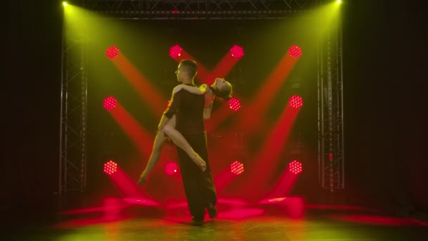 Jonge dansers die ballroom danselementen dansen. Rumba, salsa, tango, flamenco. Danspartners man en vrouw dansen hartstochtelijk in het donker tegen de achtergrond van rode spots. Langzame beweging. — Stockvideo