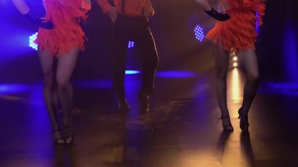 Grupo de dança vestido em trajes de estilo Chicago dos anos 30 dançando alegremente em estúdio com luzes brilhantes. Homem de chapéu e mulher em vestidos curtos realizam espetáculo teatral na festa. Fecha. Movimento lento. — Vídeo de Stock