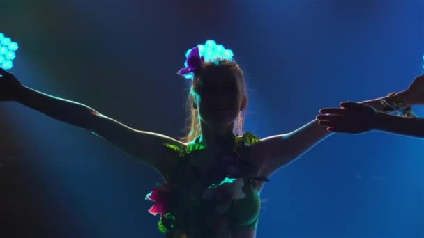 Roztomilé tanečnice tančí havajský tanec, plasticky hýbou těly a boky. Silueta žen tančících na havajském večírku luau na pozadí barevných světel. Zavřít. Zpomalený pohyb.