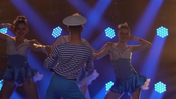 Tres mujeres guapas en trajes de marinero seductores bailan incendiariamente con su pareja en una gorra de marinero. Espectáculo de danza teatral de estilo náutico sobre el telón de fondo de las luces azules. De cerca. Movimiento lento — Vídeo de stock