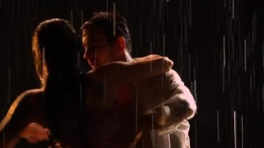 Seksi bir çift yağmurun altında müziğin ritmine göre hareket eder ve sonra suyun yüzeyine uzanır. İki âşığın siluetleri. Dansta aşk hikayesi. Stüdyoda siyah arka plan. Kapat..