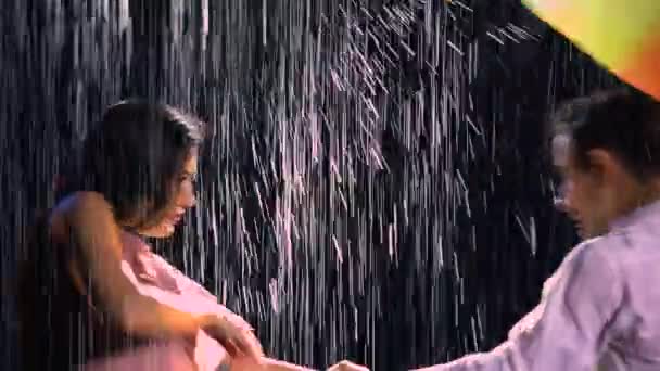 Historia miłosna pary w deszczu, wyrażona w namiętnym tańcu. Romantyczne spotkanie dwojga kochanków. Para pod jasnym, kolorowym parasolem. Mokre ciała mężczyzny i kobiety w studio miękkie światło. Zamknij się.. — Wideo stockowe
